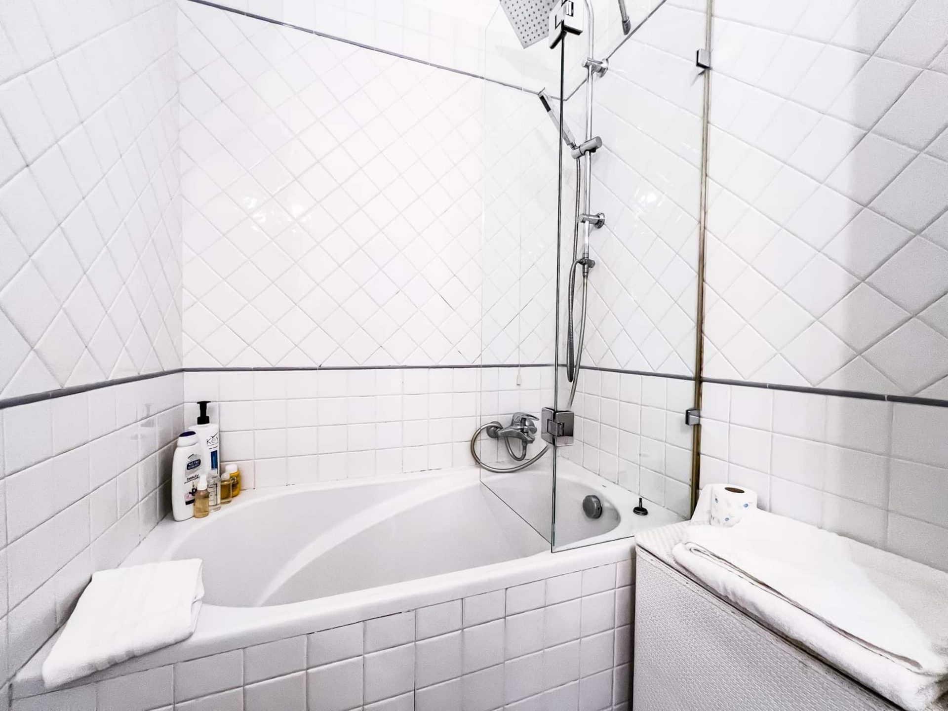 La vasca da bagno con doccia a parete, rivestita in piastrelle bianche