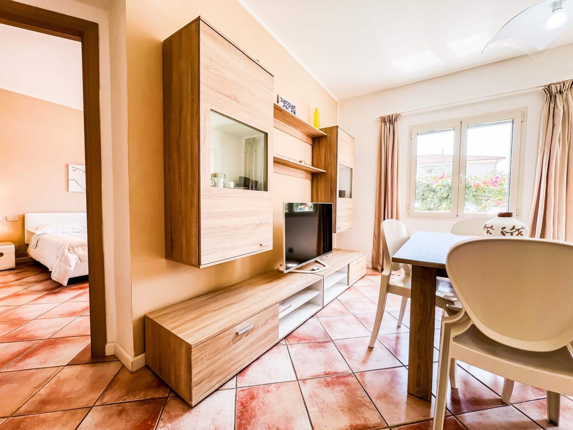 Il soggiorno di HOME FOR YOU con la parete attrezzata in legno chiaro, la TV e il tavolo da pranzo
