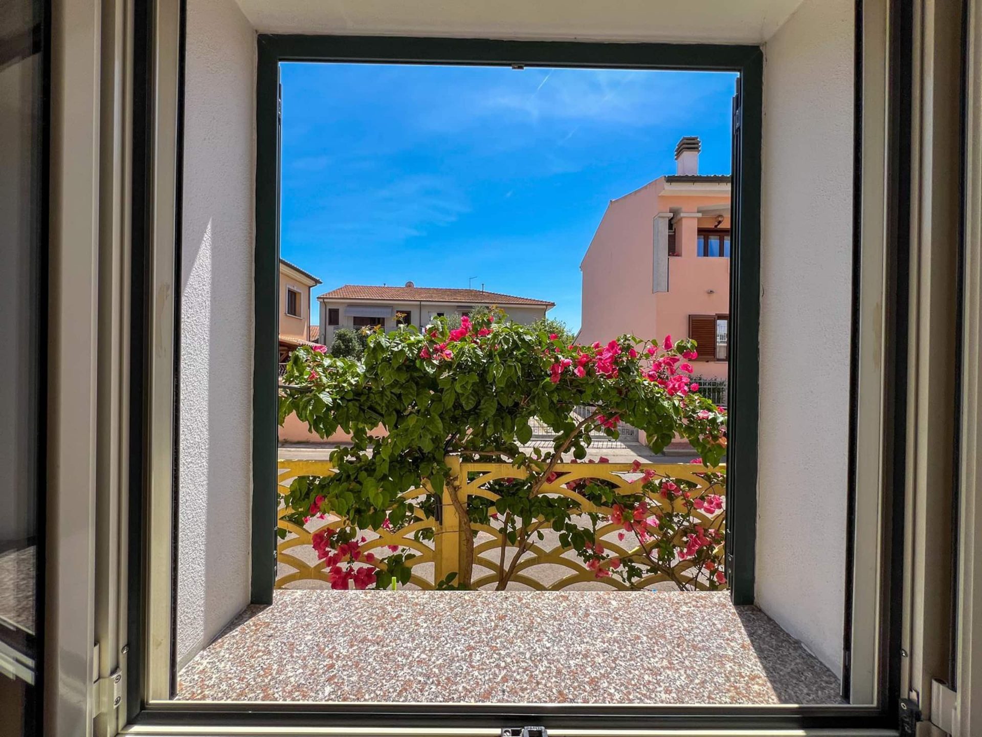 La finestra aperta sulla bougainvillea in fiore e sulle case del quartiere